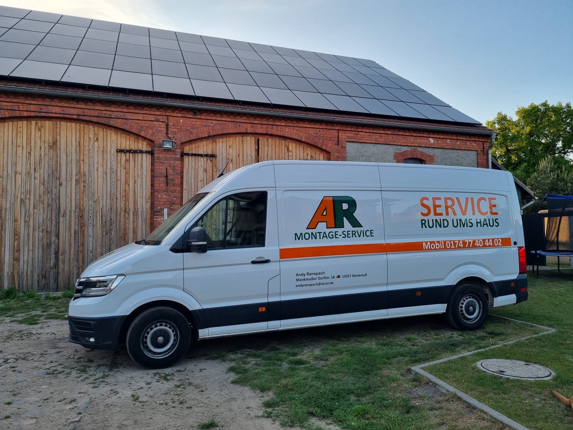 White service van with orange AR Montage Service branding parked in front of a brick barn with solar panels